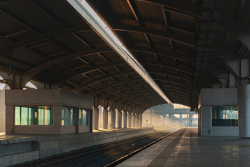 Peaceful view of an empty modern railway station platform illuminated by warm sunrise light and morning mist in urban setting.