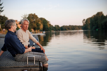 Senior friends sitting on pier with beer bottles near lake