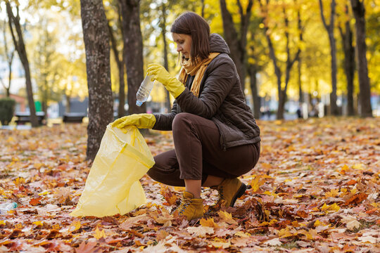 Woman cleaning autumn park with trash bag and yellow gloves