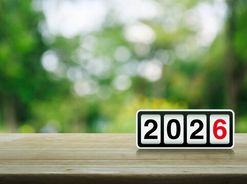 Retro flip clock with 2026 text on wooden table over blur green tree in park, Happy new year 2026 cover concept