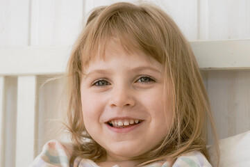 4 years girl joking, sticking tongue out with silly expression. Child making face. Funny foolishness portrait of little kid doing crazy comical gesture among a white wall. Closeup face. Low contrast