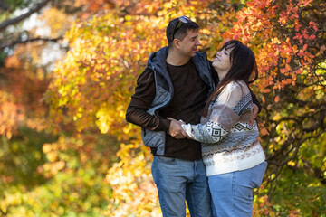 Fototapeta premium A young couple in love walks through the park with their pet. The lovers enjoy the golden autumn scenery.