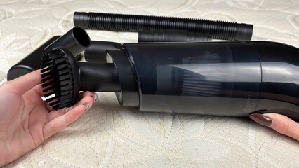 Woman's hand attaching a nozzle to a portable cordless vacuum cleaner against a white mattress....