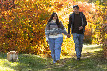 Fototapeta premium A young couple in love walks through the park with their pet. The lovers enjoy the golden autumn scenery.