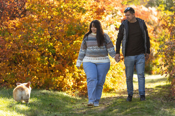 Fototapeta premium A young couple in love walks through the park with their pet. The lovers enjoy the golden autumn scenery.