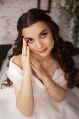 Portrait of a beautiful young woman with long dark curly hair in a white wedding dress