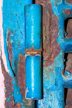 Close up of rusty blue metal door hinge with peeling paint and decay