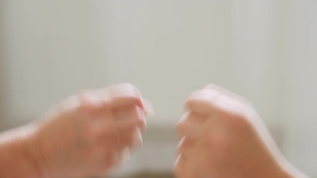 Close up of two blurred hands in fast motion while playing hand game indoors, emphasizing energy and movement during fun interaction in soft lit room with neutral background