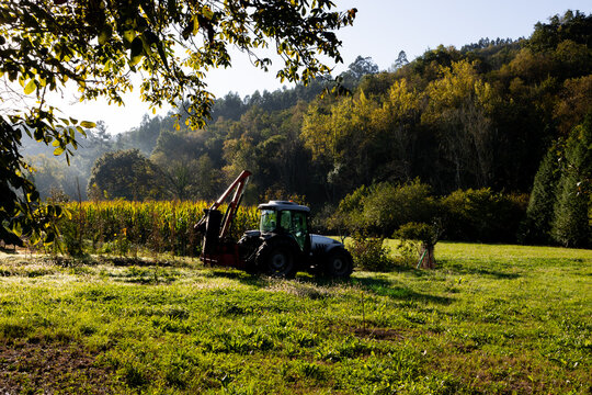 Tractor in lush green field with forested hills and blue sky