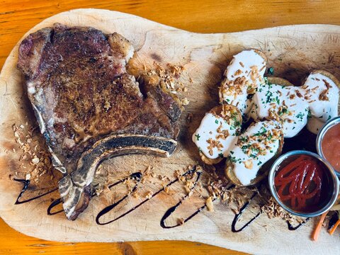 Grilled ribeye steak served with baked potatoes mixed with yogurt and assorted sauces on the side - Powered by Adobe