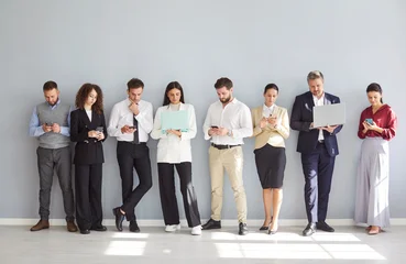 Fotobehang Sportwinkel Diverse group of business professionals standing together on a gray background, working online using phones and laptops as a team. Internet technology, and collaboration in an office setting.  © Studio Romantic