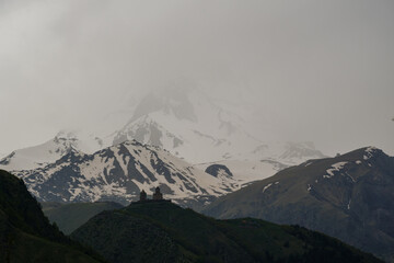 Snowy Mountain Kazbek with ancient Gergeti Trinity church Tsminda Sameba On a Green Hilltop Under Cloudy Skies