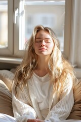 Naklejka premium A young individual sits peacefully on a soft sofa, enjoying the warm morning sunlight. Their eyes are closed, and a sense of tranquility fills the serene home environment