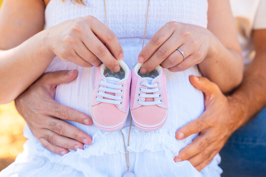 Close up of pregnant couple holding pink baby shoes on belly, concept of maternity, family love, anticipation, pregnancy and happiness, symbol of future parenthood and new life expecting baby girl