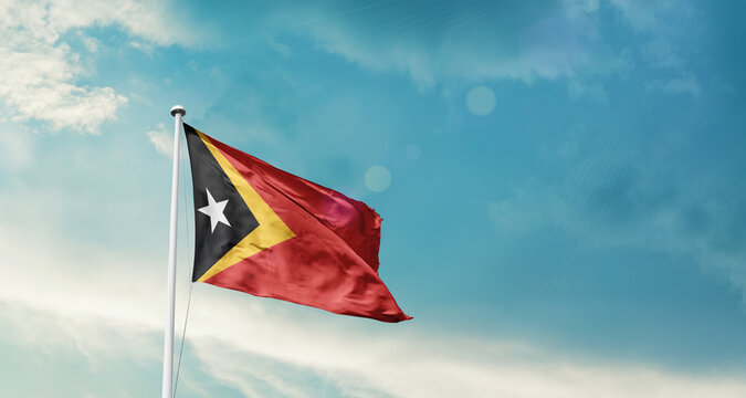 East Timor national flag fluttering. The flag blowing in beautiful soft sky. East Timor national flag for independence day. - Powered by Adobe