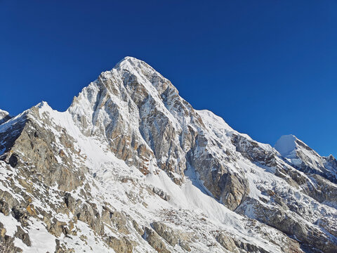 Snow-covered mountain peak rises against a bright blue sky highlighting stunning landscape. Himalayan Mountains, Nepal