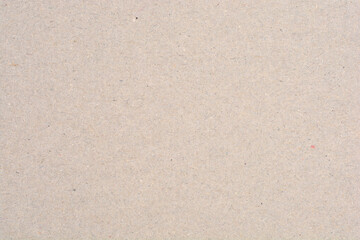 A close-up of light brown-gray recycled cardboard or heavy paper featuring a rough, uneven texture and visible small dark fiber flecks