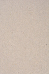 A close-up of light brown-gray recycled cardboard or heavy paper featuring a rough, uneven texture and visible small dark fiber flecks