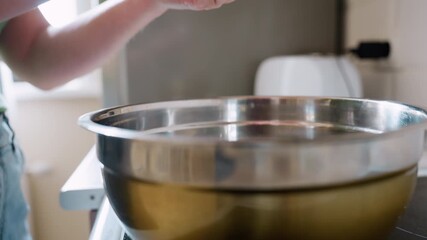 Close up of woman hand cracking fresh egg into stainless steel mixing bowl in kitchen, preparing ingredients for cooking with natural light