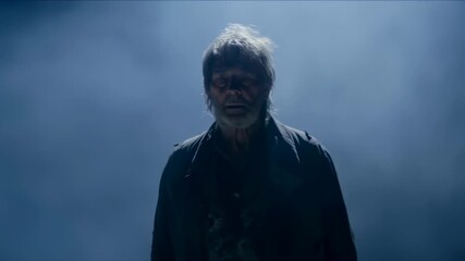 Elderly man in dark clothing, against bright background with a glow, possibly illuminated by a light