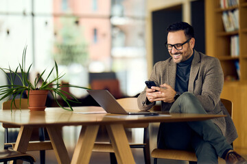 Professional Man in Blazer Uses Phone at Modern Office With Laptop and Plant