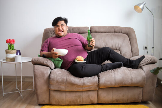 Funny Man Chows Down With Burger, Beer, and Bowl While Lounging on Sofa