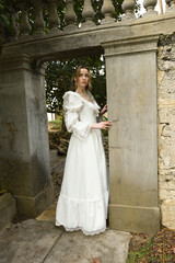 Fototapeta premium Full length female figure of beautiful blonde model wearing white fantasy wedding gown. walking through doorway of historical fairytale castle location 