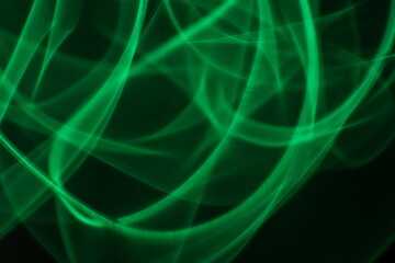 Abstract green light trails on dark background, long-exposure swirling motion lines for technology and energy background. Abstract green smoke or green fire on dark background. Green gas fire abstract