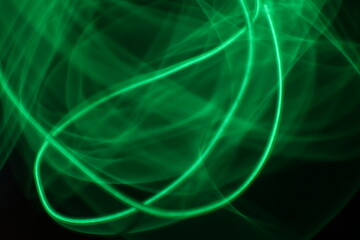 Abstract green light trails on dark background, long-exposure swirling motion lines for technology and energy background. Abstract green smoke or green fire on dark background. Green gas fire abstract