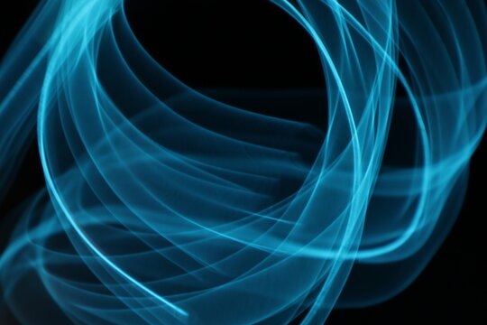 Abstract blue light trails on dark background, long-exposure swirling motion lines for technology and energy background. Abstract blue smoke or blue fire on dark background. Blue gas fire abstract art