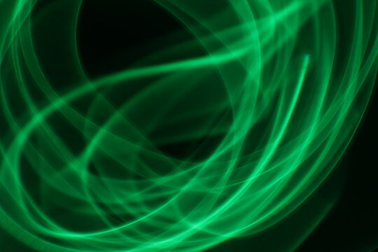 Abstract green light trails on dark background, long-exposure swirling motion lines for technology and energy background. Abstract green smoke or green fire on dark background. Green gas fire abstract