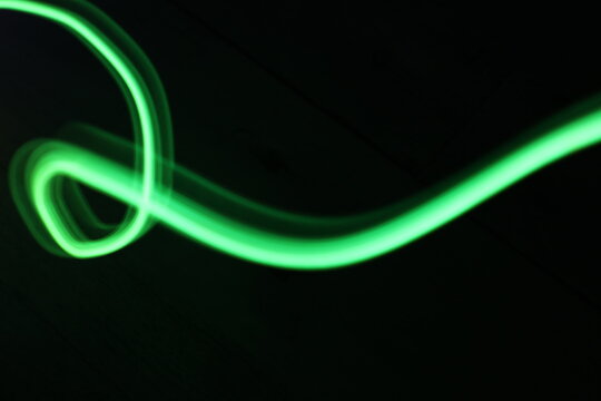 Abstract green light trails on dark background, long-exposure swirling motion lines for technology and energy background. Abstract green smoke or green fire on dark background. Green gas fire abstract