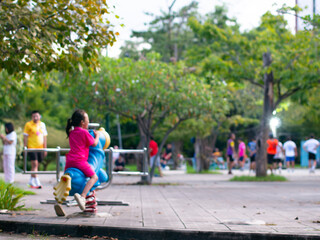Children playing on spring rider toy horse in public park with blurred people exercising in background