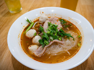 Thai Tom Yum Glass Noodle Soup with Pork Fishballs and Fresh Herbs in White Bowl