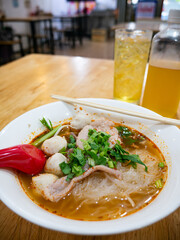 Thai Tom Yum Glass Noodle Soup with Pork Fishballs and Fresh Herbs in White Bowl