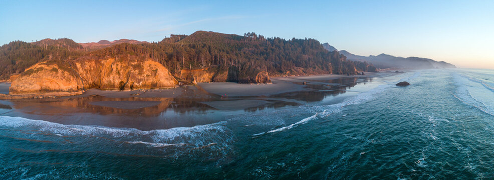 Aerial view of golden light kissing the rugged cliffs and dark green forests meeting the shimmering ocean waves along the Oregon coast, Oregon Coast, United States. - Powered by Adobe