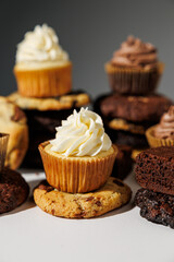 Chocolate and vanilla frosted cupcakes rest atop stacked cookies in a creative dessert arrangement on a white surface, with a blurred gray background and copy space