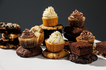 Artistic arrangement of chocolate and vanilla cupcakes, stacked cookies, and fudgy brownies on a white pedestal with a gray backdrop and copy space