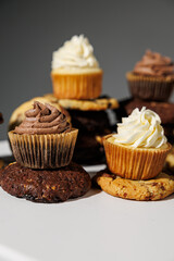 Chocolate and vanilla frosted cupcakes rest atop stacked cookies in a creative dessert arrangement on a white surface, with a blurred gray background and copy space