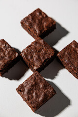 Overhead view of five rich chocolate brownies arranged in a cross pattern on a white surface with dramatic shadows and copy space