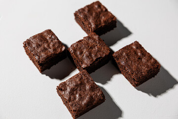 Overhead view of five rich chocolate brownies arranged in a cross pattern on a white surface with dramatic shadows and copy space