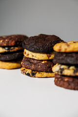 Close-up image of stacked cookies in various flavors including chocolate chip, double chocolate, and cookies and cream, arranged on a white surface with a soft gray background