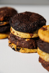 Close-up image of stacked cookies in various flavors including chocolate chip, double chocolate, and cookies and cream, arranged on a white surface with a soft gray background