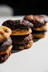 Close-up image of stacked cookies in various flavors including chocolate chip, double chocolate, and cookies and cream, arranged on a white surface with a soft gray background