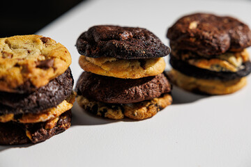 Close-up image of stacked cookies in various flavors including chocolate chip, double chocolate, and cookies and cream, arranged on a white surface with a soft gray background