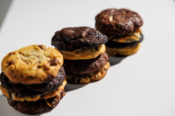 Close-up image of stacked cookies in various flavors including chocolate chip, double chocolate, and cookies and cream, arranged on a white surface with a soft gray background