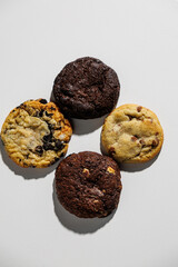 Overhead view of four different cookies—chocolate chip, double chocolate, chocolate chunk, and cookies and cream—arranged neatly on a white surface with copy space