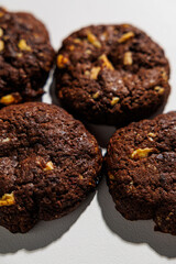 Four rich, dark chocolate cookies with visible nut chunks are arranged closely on a white background, emphasizing texture and ingredients. No branding is visible