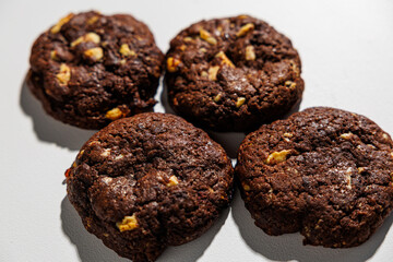 Four rich, dark chocolate cookies with visible nut chunks are arranged closely on a white background, emphasizing texture and ingredients. No branding is visible