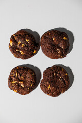A flat lay of four dark chocolate cookies with visible nut chunks, arranged neatly on a white surface. No branding or packaging is visible